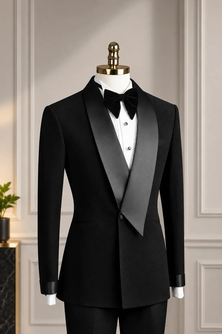 A black tuxedo jacket with satin peak lapels, displayed on a white mannequin torso wearing a white dress shirt and black bow tie, set against a light beige paneled wall.