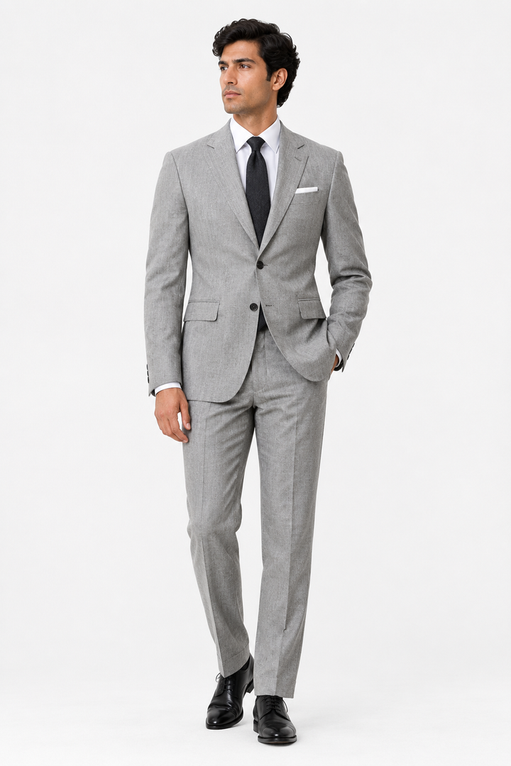 A man modeling James Bond-inspired light gray two-piece suit with a subtle micro-check pattern, paired with a white dress shirt, black tie, and white pocket square, on a solid white studio background.