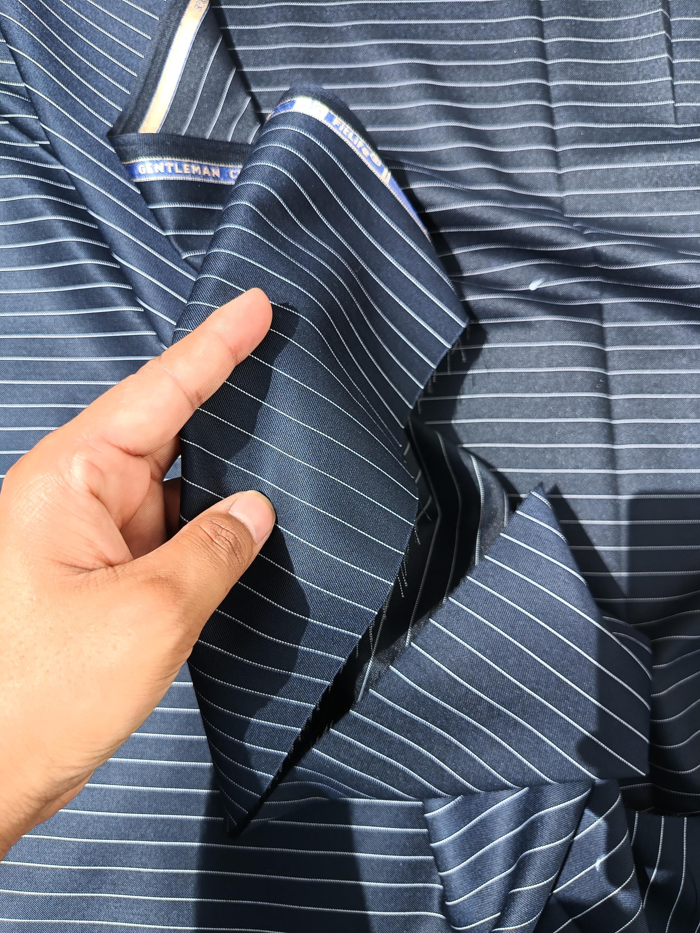A close-up of a navy blue pinstripe suiting fabric with a hand holding up to show the fabric texture and stripe pattern.