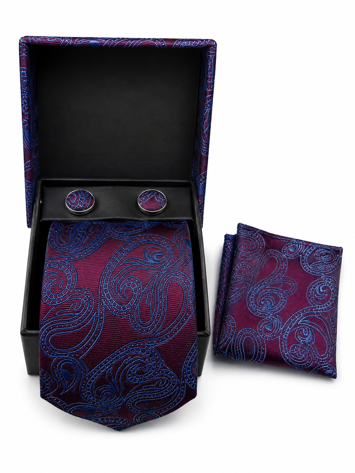 A men's necktie and matching pocket square set with round cufflinks, displayed in an open black gift box on a white background. The fabric features a detailed paisley pattern in deep burgundy and bright blue.