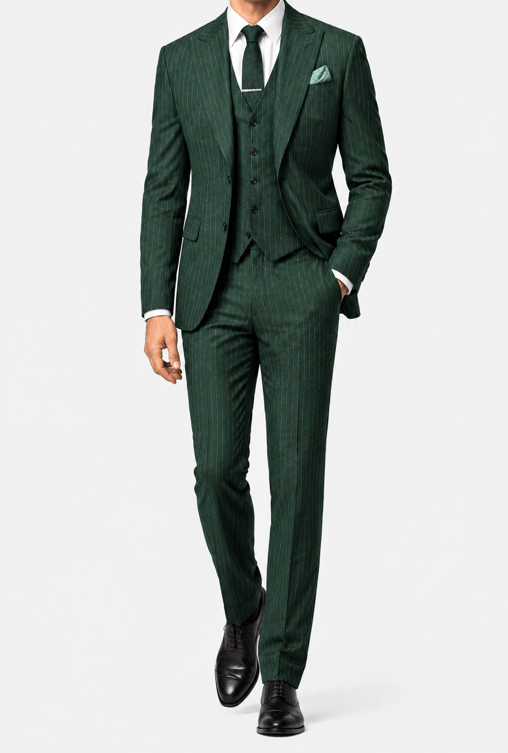 A man wearing a  pinstripe PeakyBlindersSuit three-piece suit with a matching vest and trousers, a white dress shirt, a dark green tie, and black dress shoes, photographed against a light gray studio background.