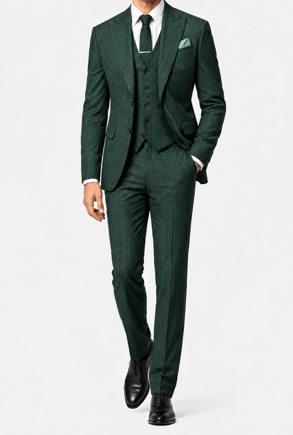 A man wearing a  pinstripe PeakyBlindersSuit three-piece suit with a matching vest and trousers, a white dress shirt, a dark green tie, and black dress shoes, photographed against a light gray studio background.